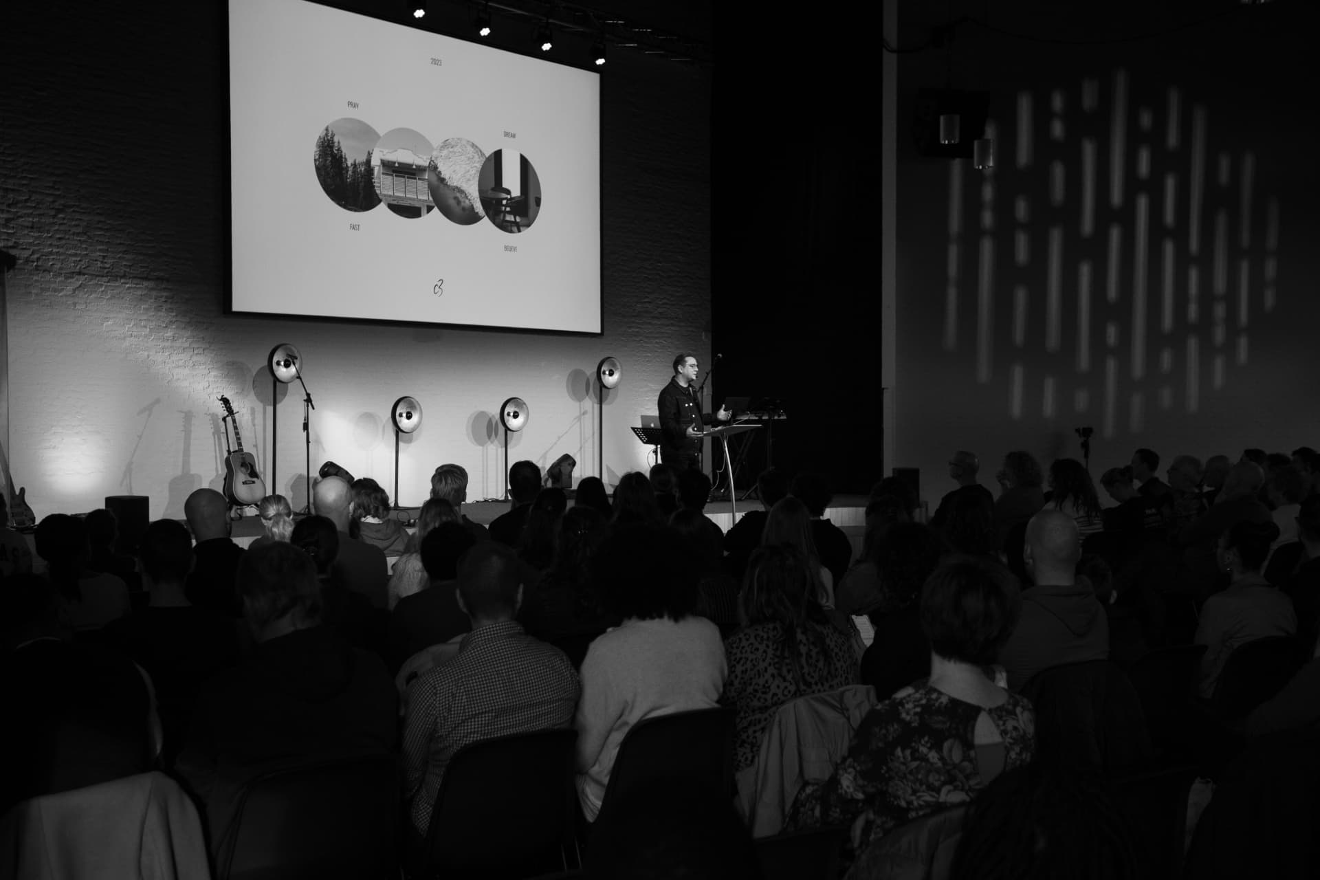 Spreker op het podium met de volle zaal tijdens de preek